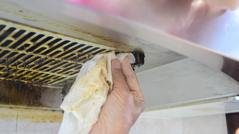 A close-up of someone in protective gloves cleaning a dirty vent with a disposable wipe