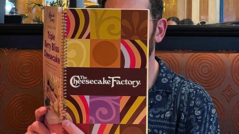 Man holding The Cheesecake Factory menu in front of his face