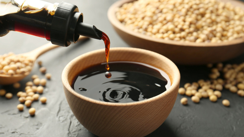 A close-up of soy sauce being poured from a bottle into a small wooden bowl
