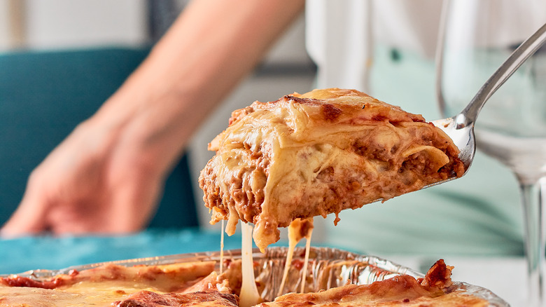 scooping slice of lasagna from baking dish
