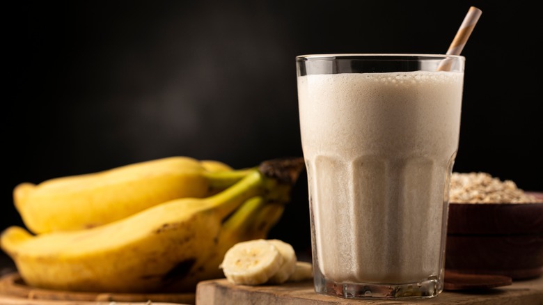banana oat smoothie on a wood cutting board with banana bunch in the background