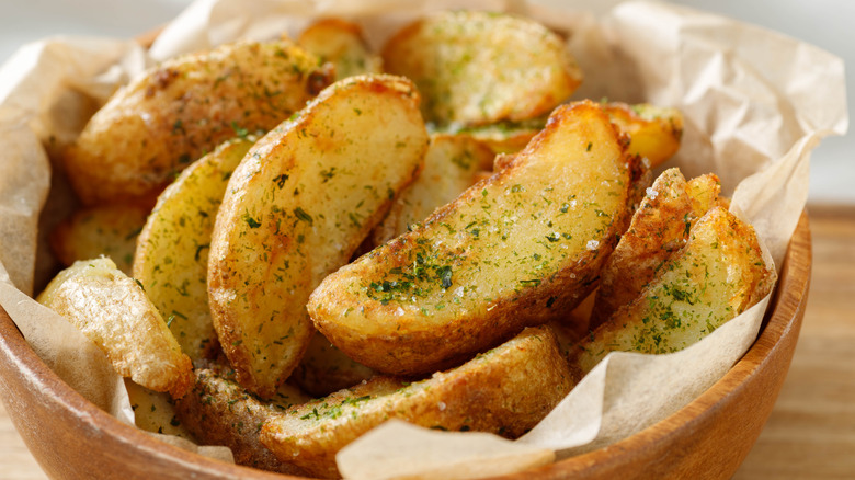 Fried potato wedges in paper-lined bowl with seasoning