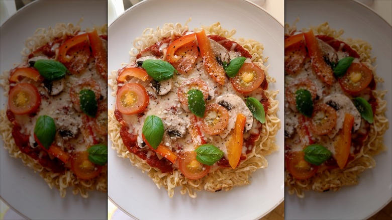 Overhead shot of ramen pizza with fresh tomatoes and basil.