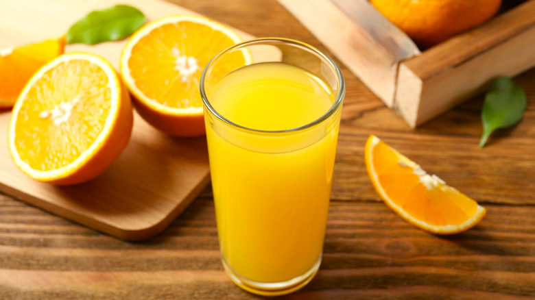A glass of orange juice with some cut oranges on a cutting board