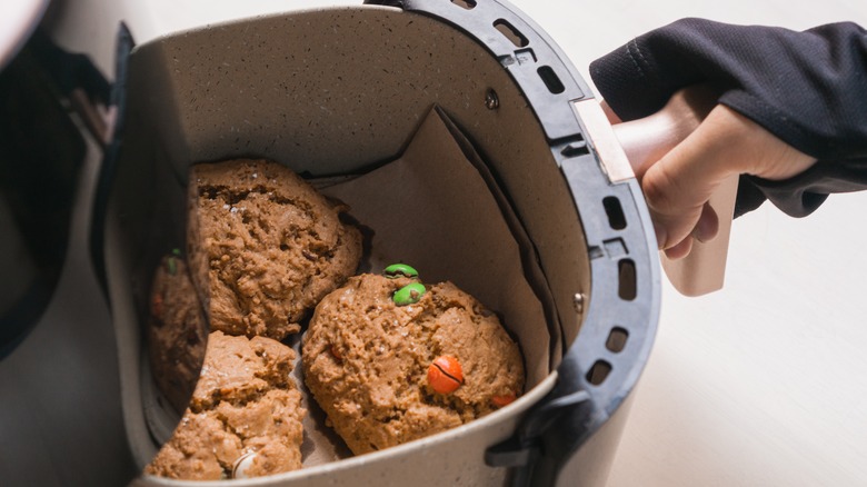 Hand pulling out air fryer basket containing chocolate cookies