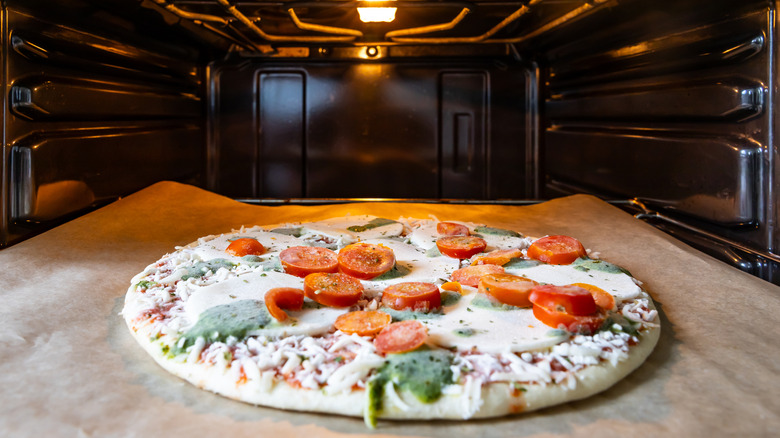 A frozen pizza sitting on a baking sheet about to go in an oven