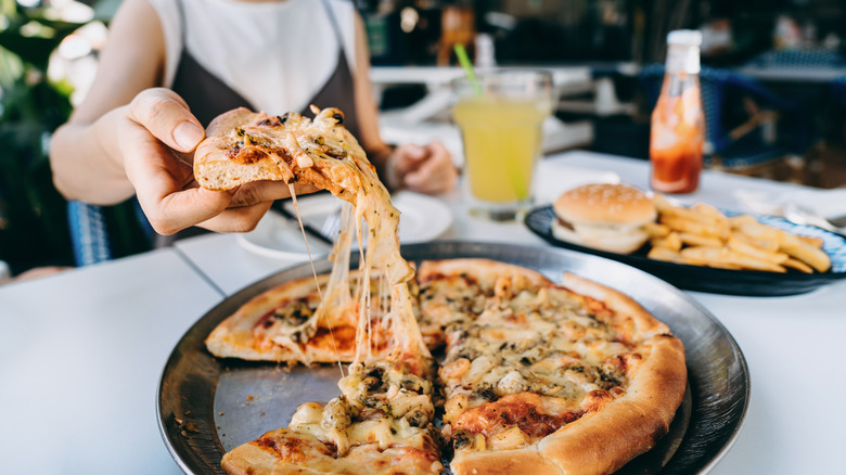 Someone lifting a slice from a pizza, with cheese still connecting the slice