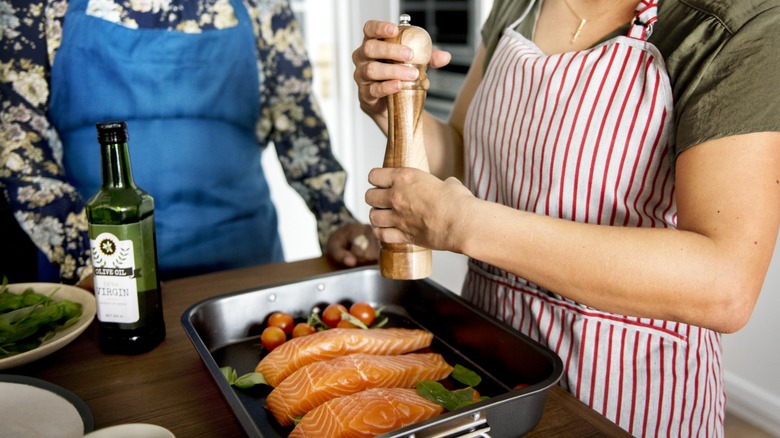 seasoning salmon in pan with pepper and tomatoes