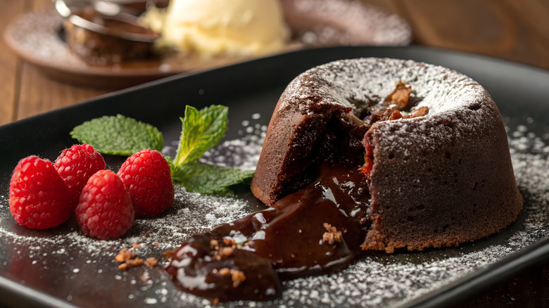chocolate lava cake with chocolate spilling out the center and raspberries next to it.