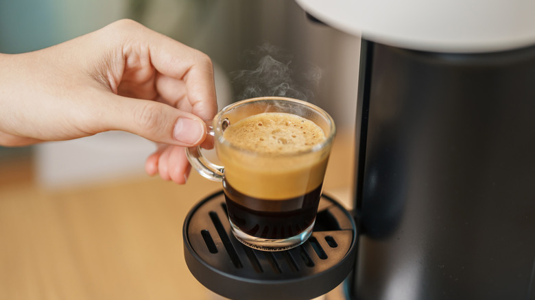 woman's hand holding a tiny cup of coffee from a single serve coffee machine