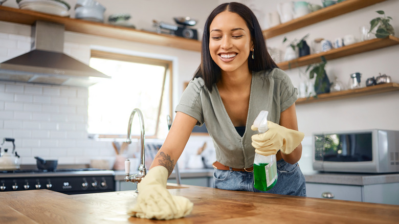 Someone smiling while they clean their kitchen countertop next to a sink
