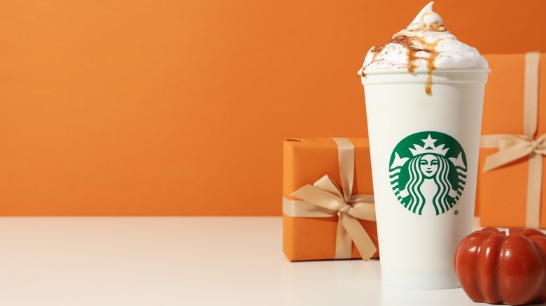 A cup of Starbucks coffee with pumpkin and present wrapped in orange paper.