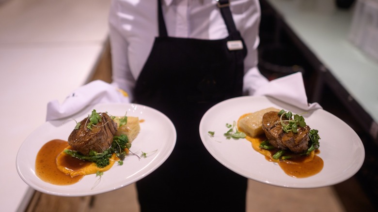 server holds two dishes of juicy filet mignon