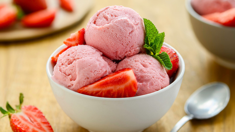 Closeup of strawberry ice cream in white bowl with mint leaves.