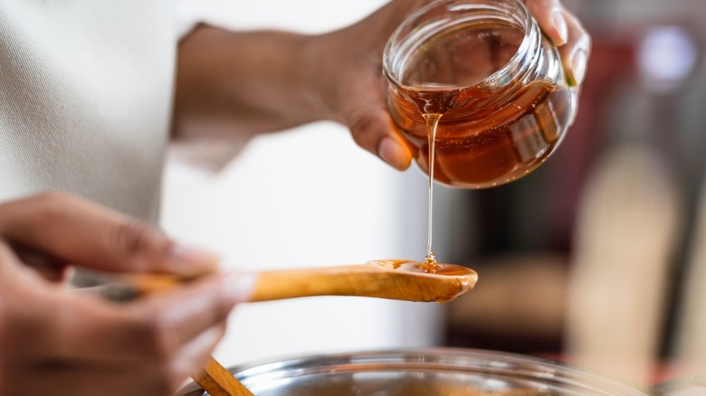 Person pouring honey onto spoon over bowl