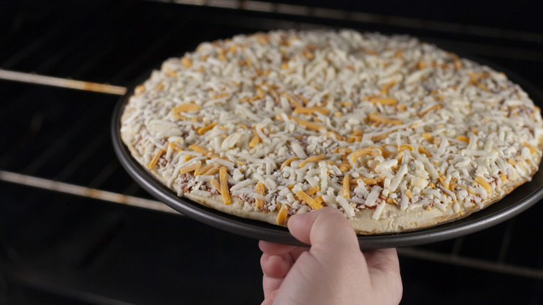 Hand puts frozen pizza on pan into oven