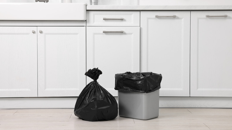 Small silver trashcan and black trashbag on floor of kitchen.