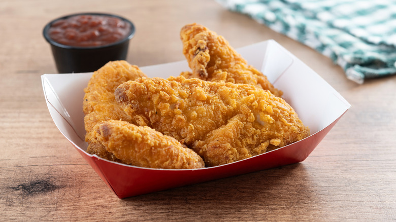 Paper basket with fried chicken fingers and cup of ketchup