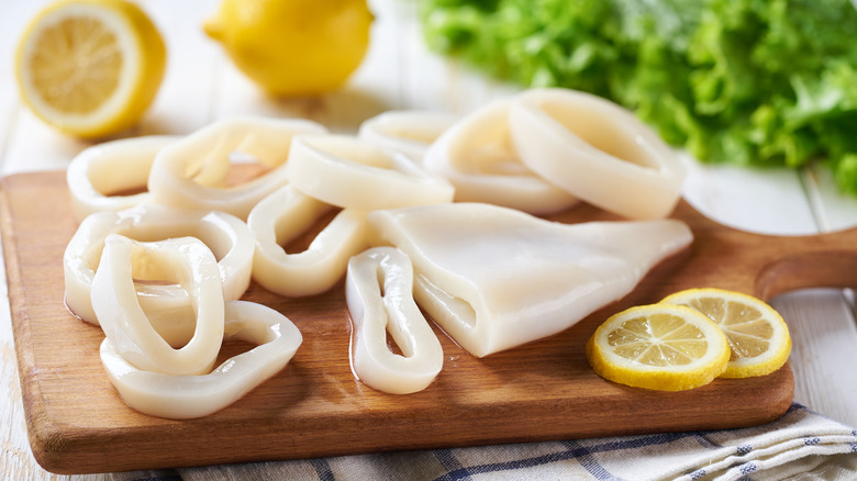 Raw squid partially cut into rings on a wooden cutting board with lemon slices