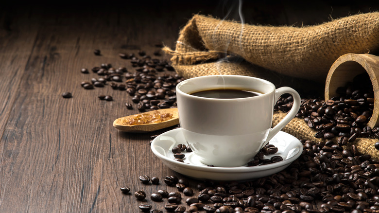 Cup of coffee with coffee beans and burlap in background on wood table