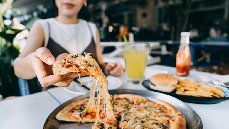 A person grabs a cheesy slice of pizza from a pan