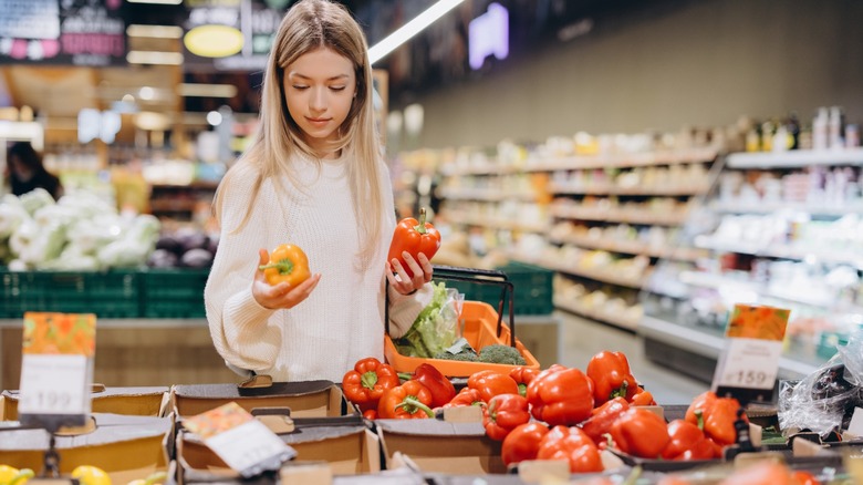 young woman examines two bell peppers at grocery store