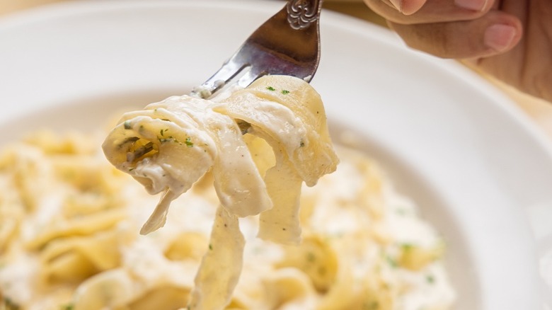 Fork twirling noodles from plate of fettuccine alfredo
