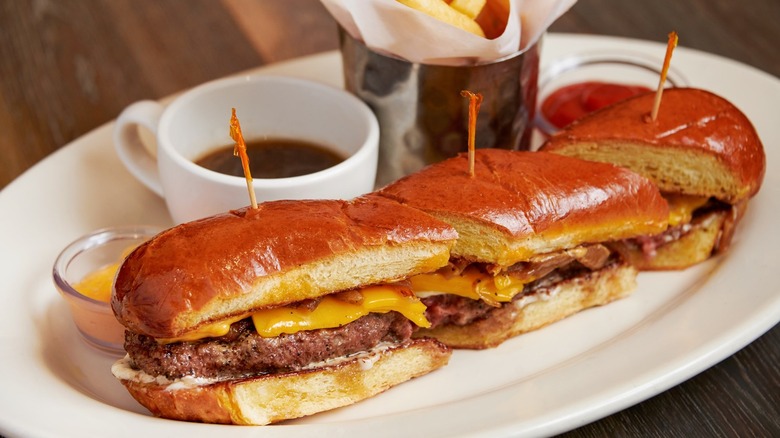 Sliced up French Dip cheeseburger on plate with fries