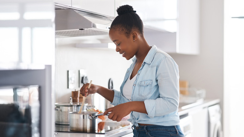 Smiling woman stirs contents of a saucepan.