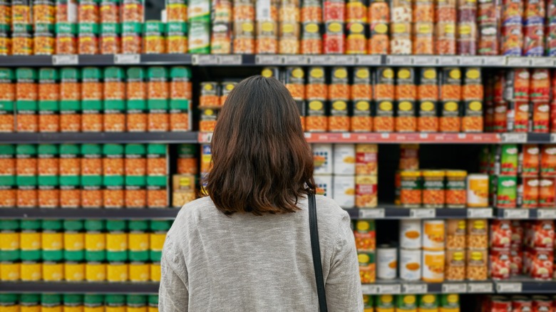 Woman looking at canned food section at grocery store.