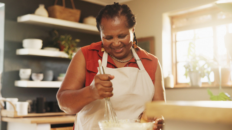 Woman in kitchen smiling while mixing something in bowl.