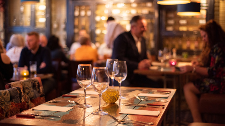 Diners inside steakhouse with table and wineglasses in foreground.
