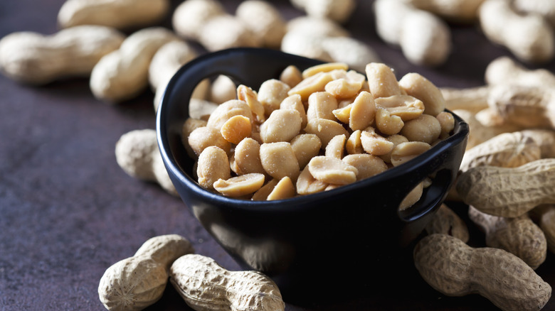 Salted shelled peanuts in a bowl with unshelled peanuts in background and foreground