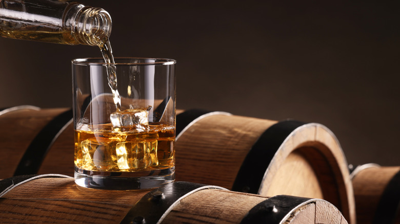 Pouring whiskey from bottle into glass on wooden barrel