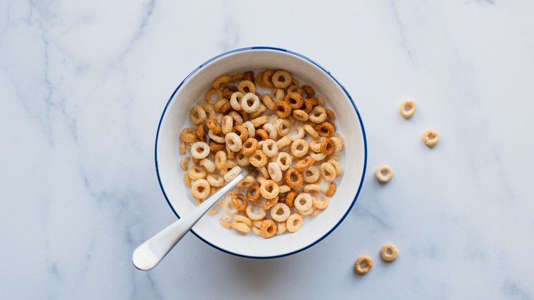 a bowl of cheerios with a spoon on a marble table