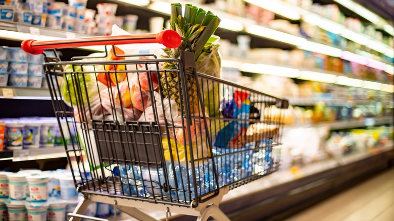 Shopping cart with food items in a grocery aisle.