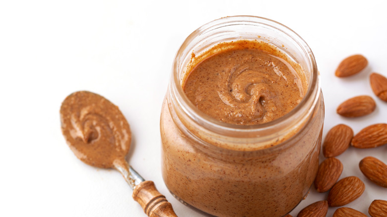 A jar of almond butter with a spoon and raw almonds