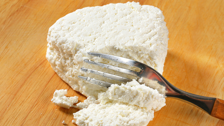 A piece of cottage cheese on a chopping board with fork