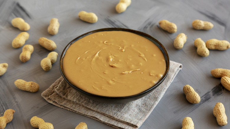 Bowl of peanut butter surrounded by peanuts in the shell