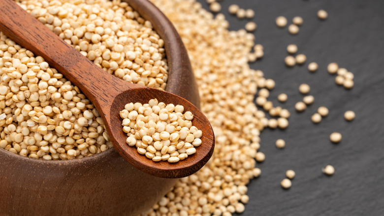 Raw quinoa grains in a wooden bowl next to a wooden spoon