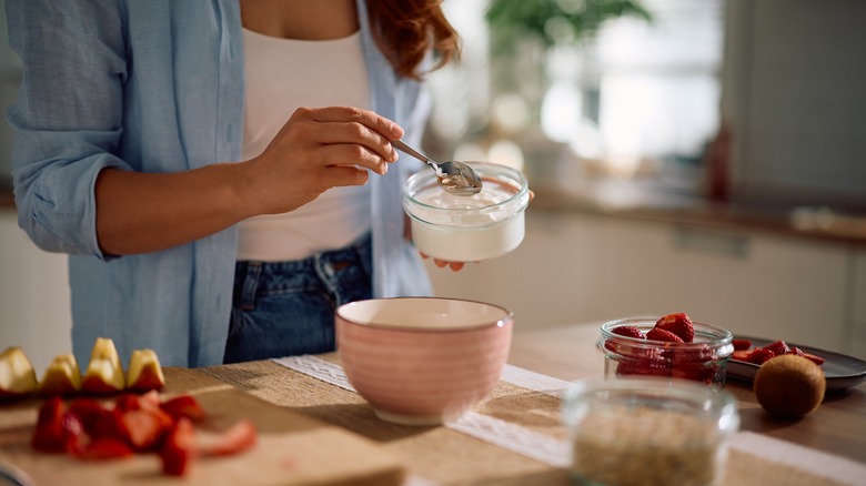 Person scooping Greek yogurt from a glass container.