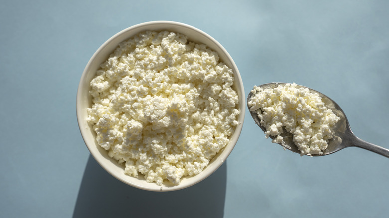 Overhead view of cottage cheese in white bowl, blue background.