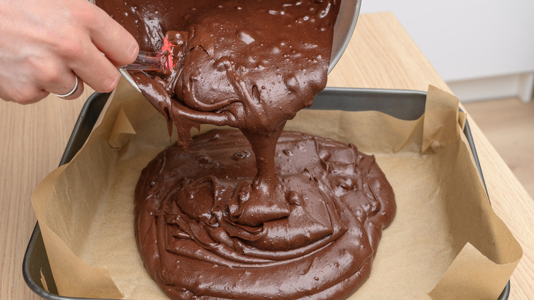 Closeup of person pouring brownie pattern in parchment paper-lined pan.