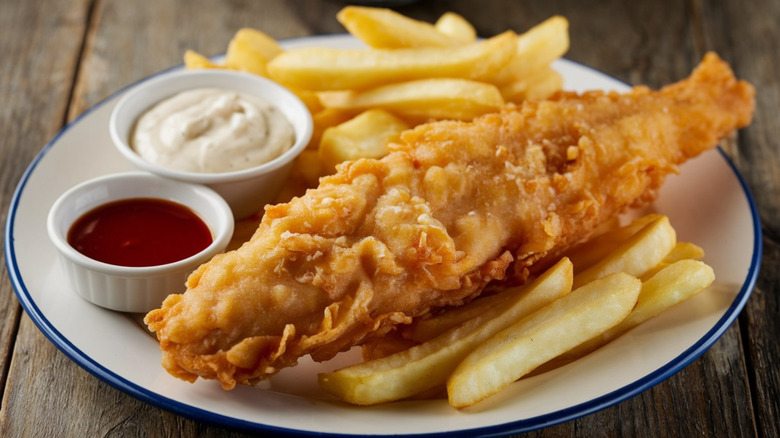 A plate of crispy, fried fish with fries and sauces