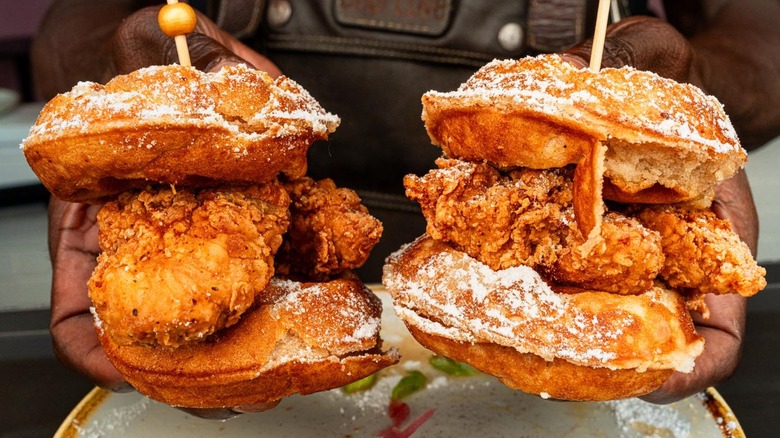 Someone holding two fried chicken waffles from Chick 'N Jones