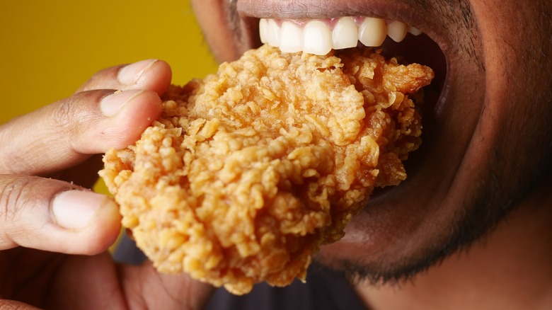Someone biting into a piece of fried chicken