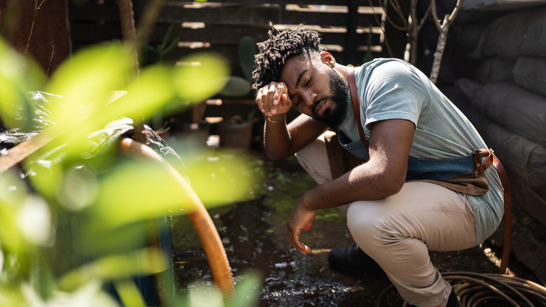 Man wipes forehead while working in garden