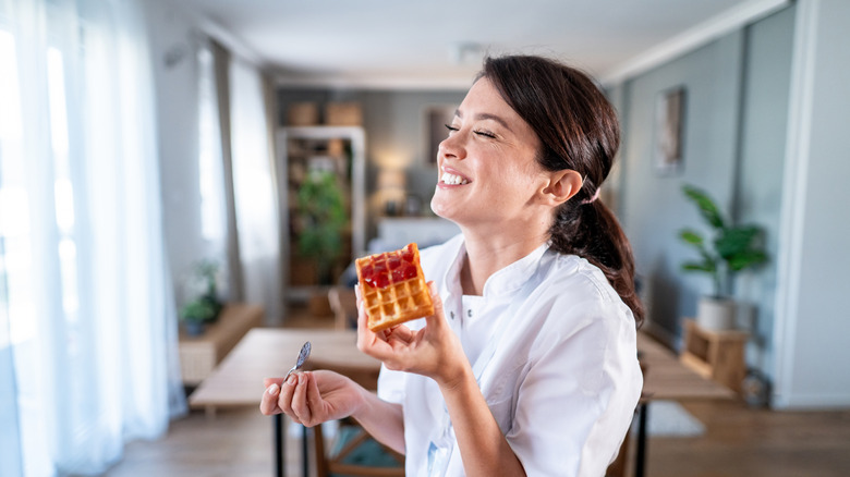 Woman smiling in kitchen while eating waffle