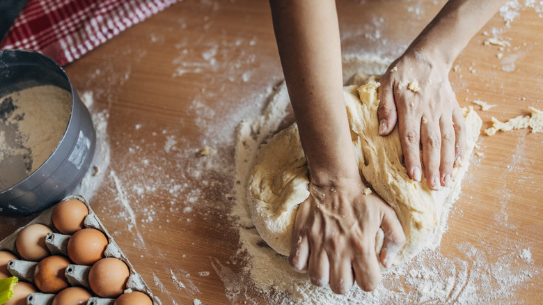 Hands knead dough on a wooden surface
