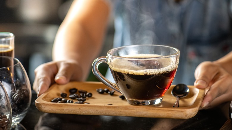 Black drip coffee being served in a glass cup.